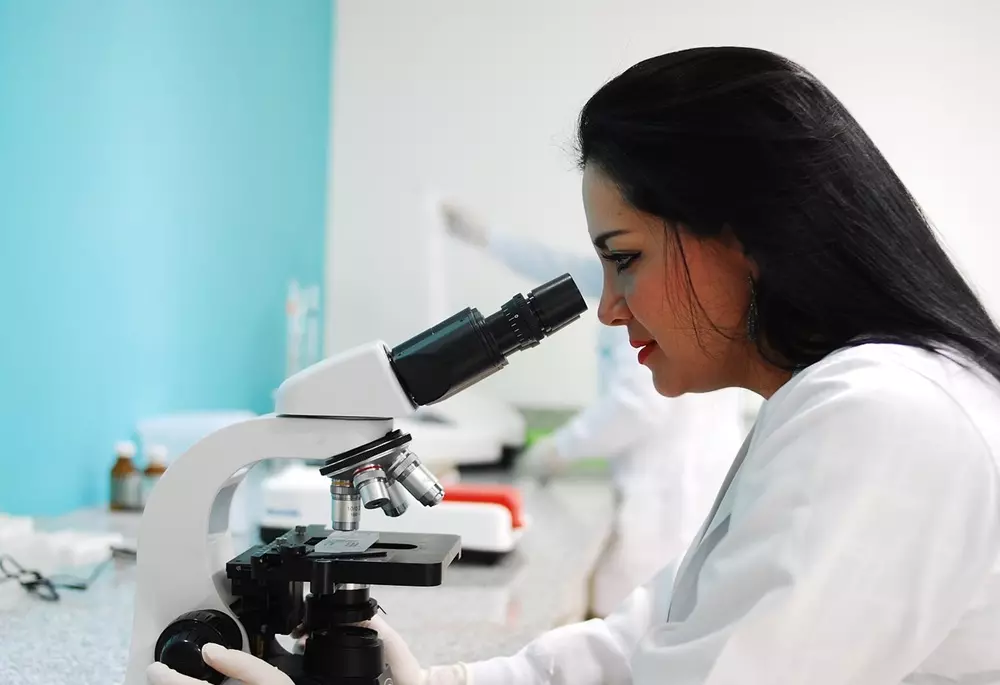 Kobieta przed mikroskopem wykonująca mikrobiologiczne badanie wody pod kątem Legionelli